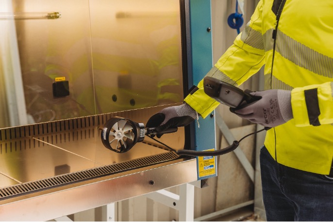 Armstrong Environmental specialist measuring airflow at an LEV enclosure using a rotating-vane anemometer