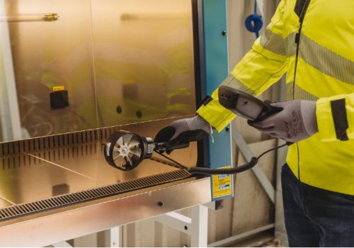 Armstrong Environmental specialist measuring airflow at an LEV enclosure using a rotating-vane anemometer